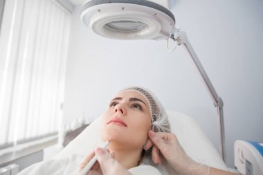 Estetik ameliyattan önce yüzünde delinme izleri olan güzel bir genç kadın. Güzellik uzmanı kadın yüzüne dokunuyor