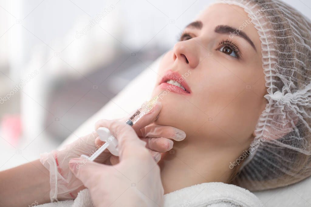 Hands of cosmetologist making injection in face, lips. Young woman gets beauty facial injections in salon. Face aging, rejuvenation and hydration procedures. Aesthetic cosmetology