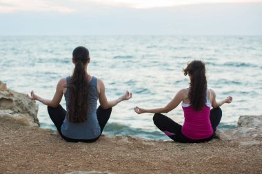 Gün batımında plajda yoga yapan iki kız.