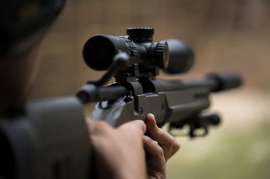 Keskin nişancı dürbünden bakarak tüfeği ateşliyor.