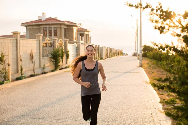 Vacker kvinna som springer i solnedgången. Ung sportig kvinna som springer i staden vid solnedgången. Bakifrån sportig flicka som arbetar vid vattnet. — Stockfoto