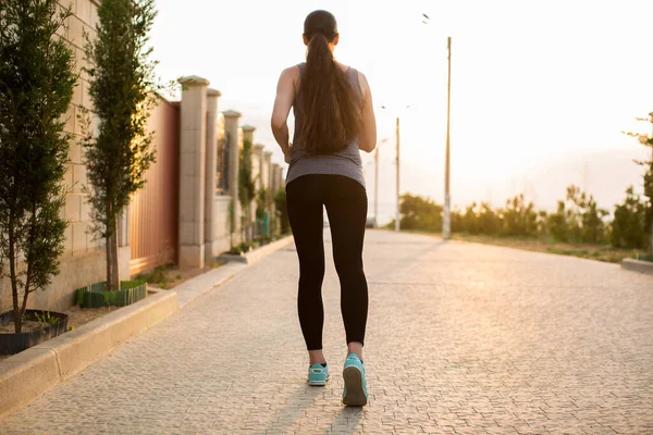 Young sporty woman running in the city at sunset. Rear view sporty girl working on the waterfront. — Stock Photo, Image