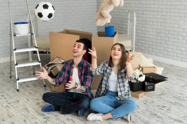 Yeni bir evde genç bir çift büyük kutuların arkasında dinleniyor. Topu at ve oyuncak ayı.