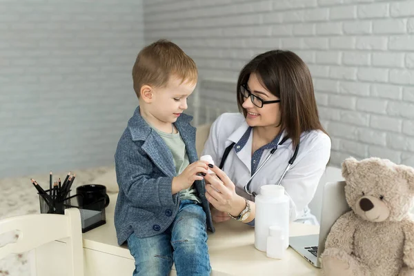 Schön lächelnde Ärztin hält Tablettenflasche in den Armen und bietet sie Kinderbesuchern in Großaufnahme an — Stockfoto