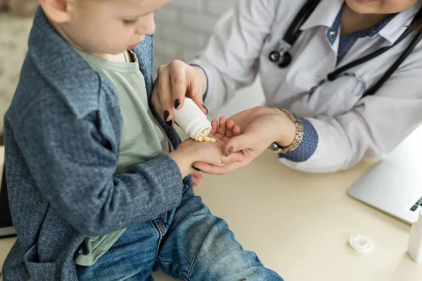 Gyönyörű mosolygós női orvos tartsa a karját tablettát üveget, és felajánlja, hogy a gyermek látogató közelkép — Stock Fotó