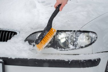 Kışın arabadan karı temizleyen kadın. Arabanın farları.