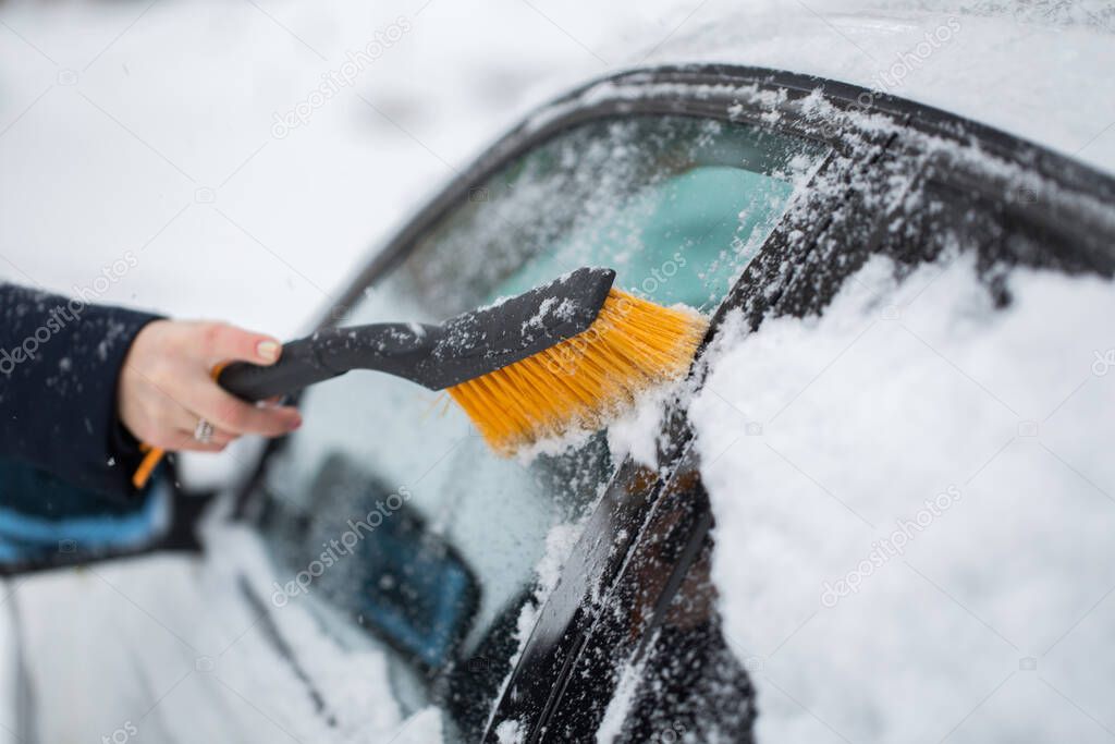 Woman cleaning snow from the car in the winter.