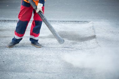 Yol işçisi asfalt yolu kesiyor, yol yenileme üzerinde çalışıyor. Toz tutsun diye asfaltı suyla kestiğini gördüm..