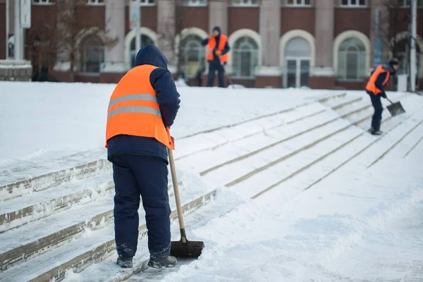 Los trabajadores barren la nieve del camino en invierno, limpiando el camino de la tormenta de nieve . — Foto de Stock