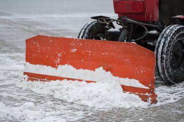 Traktör kardan yolu temizliyor. Kazıcı şehirdeki büyük miktardaki karları temizliyor..