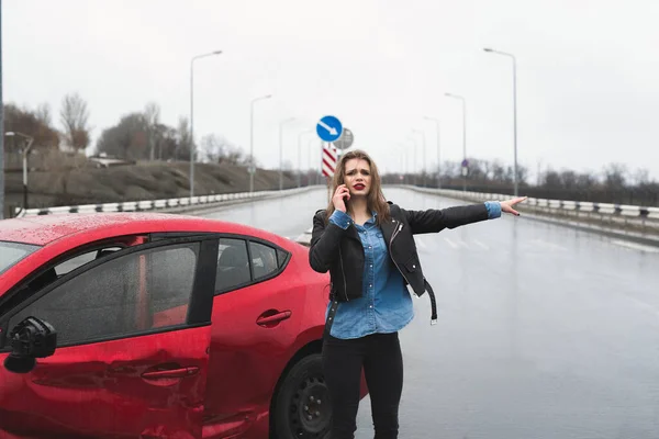 Una mujer llama a un servicio de pie junto a un coche rojo. Hermosa mujer atrapa el coche . —  Fotos de Stock