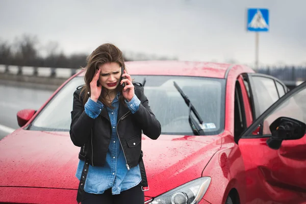 Mujer llama a un servicio de pie junto a un coche rojo . — Foto de Stock