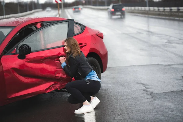 Mulher senta-se perto de um carro quebrado após um acidente. Pede ajuda. seguro automóvel . — Fotografia de Stock