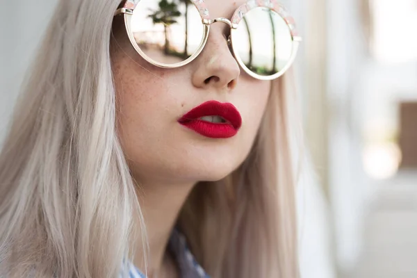 Retrato de una chica rubia bonita con el pelo largo posando a la cámara en la calle. Ella lleva vestido azul y gafas . — Foto de Stock