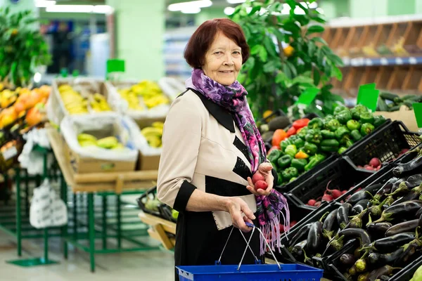 Grandma, the old woman chooses red radishes in the supermarket.