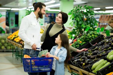 Sebze pazarında alışveriş yaparken sebze seçen bir adam ve çocuğu olan bir kadın..