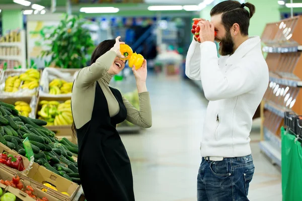 Retrato de um casal saudável olhando para frutas e legumes no supermercado enquanto faz compras. Casal alegre se entrega a produtos no supermercado . — Fotografia de Stock