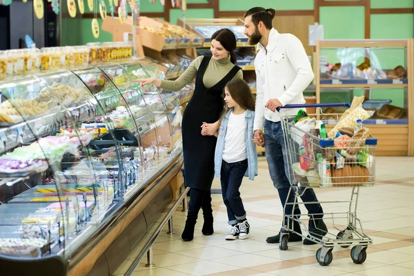 Молодая семья с ребенком выбирает десерт в окне большого супермаркета . — стоковое фото
