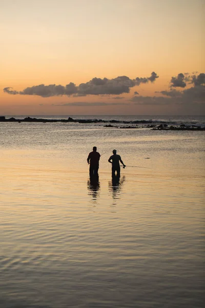 Two men fishing in the ocean from the beach at sunset. — Stock Photo, Image