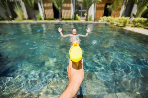 Mann feuert mit Wasserpistole auf Frau und amüsiert sich im Pool. — Stockfoto