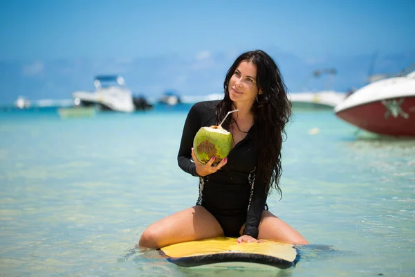 Портрет красивої дівчини-серфінгу з зеленим кокосовим горіхом з пальми сидить на жовтій дошці для серфінгу . — стокове фото