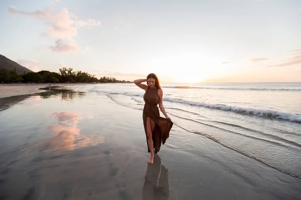 Mooie vrouw op zonsondergang achtergrond. Kleurrijke dageraad boven de zee. Zorgeloze vrouw die geniet van de zonsondergang op het strand. Gelukkige levensstijl. — Stockfoto