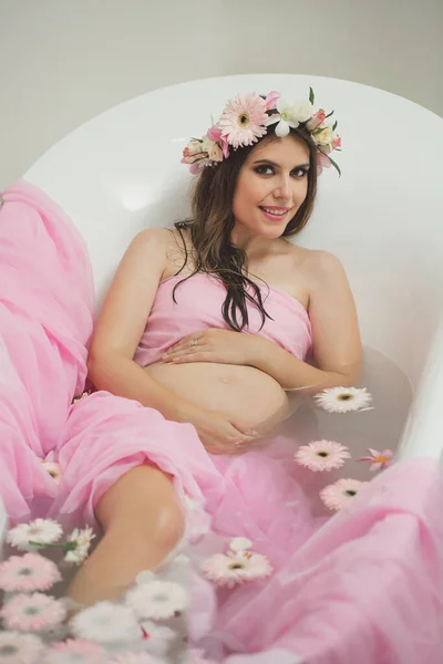 Gyönyörű terhes nő egy fürdőszobában tejjel és virágokkal. — Stock Fotó