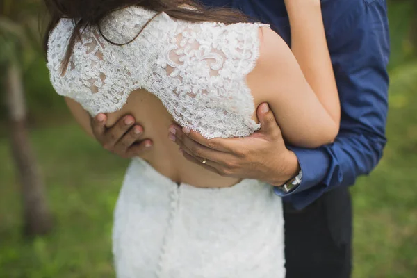 Braut und Bräutigam umarmen sich aus nächster Nähe vor dem Hintergrund grünen Grases. — Stockfoto
