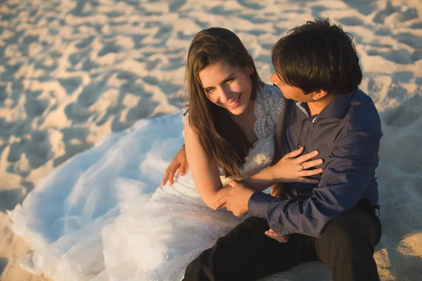 Bride and groom sit on the sand. — Stock Photo, Image