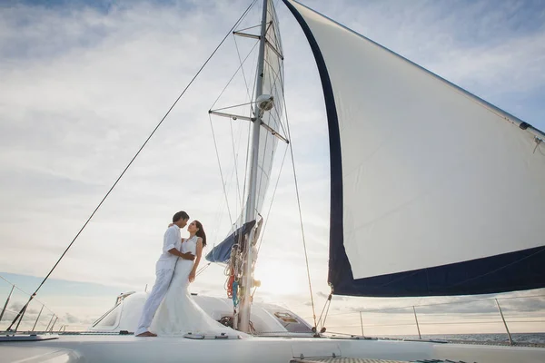 Gyönyörű házaspár menyasszony és vőlegény a jachton az esküvő napján a szabadban a tengerben. Boldog házaspár csókolózik a hajón az óceánban. Stílusos tengeri esküvő. — Stock Fotó