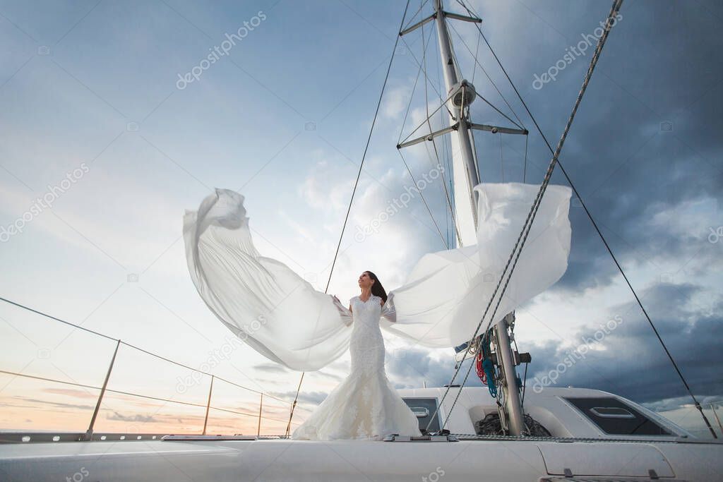 Happy bride on a yacht. White yacht with sail set goes along the island.