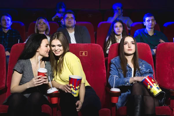 Молодые женщины смотрят кино в кинотеатре, смеются, разговаривают, едят попкорн и пьют колу — стоковое фото