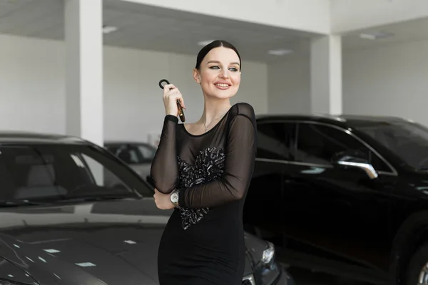 Mulher bonita ou carro vendedor stand segurando uma chave remota carro novo em um showroom carro — Fotografia de Stock