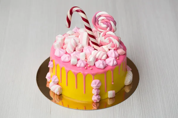 Dětský žlutý dort s růžovou polevou, meringue a bonbóny. — Stock fotografie