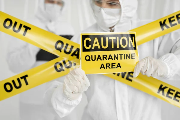 Epidemiologists a man and a woman in protective clothing are in a restricted area with a danger sign. Yellow line Keep Out Quarantine. Entrance is forbidden in quarantine zone. Coronavirus, covid-19. — Stock Photo, Image