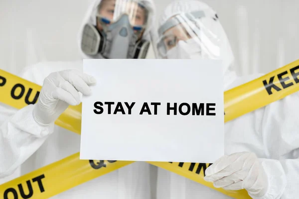 Médecins épidémiologistes homme et femme tiennent affiche avec signe Stay At Home sur fond blanc. Ligne jaune Garder hors quarantaine — Photo