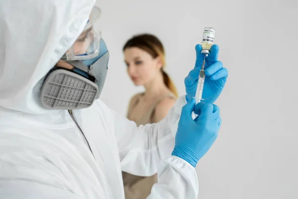 Arzt in Schutzanzug und Maske hält Spritze und Impfstoff COVID-19 in der Hand. Mann im Schutzanzug gibt einer Frau eine Spritze gegen das Coronavirus. — Stockfoto