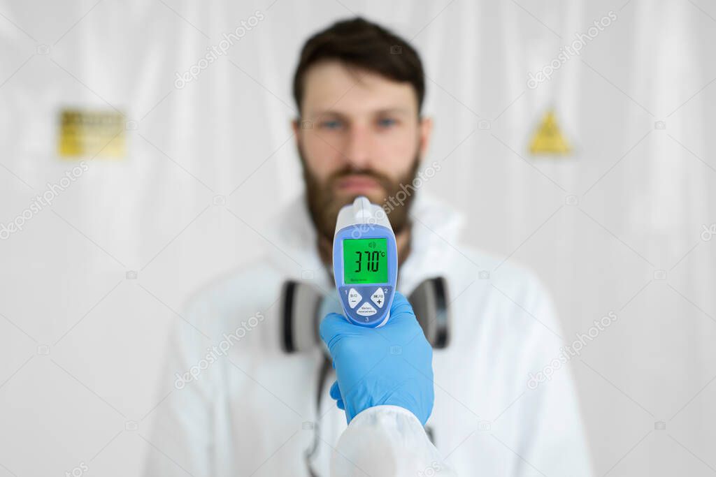 Doctor measures the temperature with an infrared thermometer to his colleague of infectious diseases. Portrait of a man doctor scientist in a lab coat. Concept of coronavirus