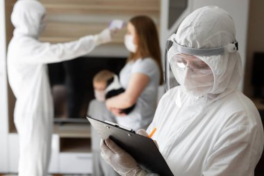 Doktor, evde kızılötesi alın termometresi kullanarak hastanın vücut ısısını ölçün. Doktor verileri bir tablete kaydediyor.