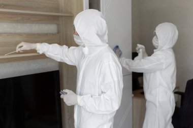 Virologlar, koruyucu giysiler içindeki insanlar evdeki dezenfeksiyonu gerçekleştiriyorlar. Mobilyaları silin ve bir koronavirüs salgını sırasında yüzeyden kirlilik için örnek alın. Covid - 19