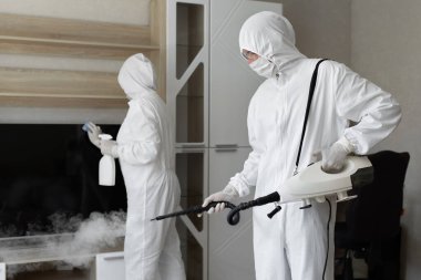 Coronavirus dezenfeksiyonu. Tehlikeli maddeler kullanan insanlar dezenfekte yapıyor. Fotokopi odası, sıcak buhar temizleme.