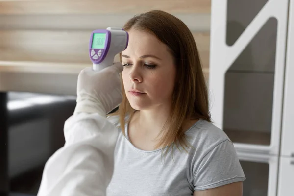 Doktor, evde kızılötesi alın termometresi kullanarak hastanın vücut ısısını ölçün. Coronavirus, covid-19, karantina, yüksek sıcaklık.