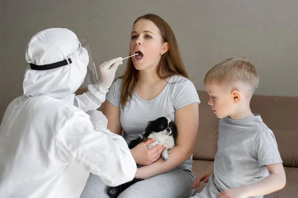 Medizintechniker in voller Schutzkleidung entnimmt im Rahmen der Operationen einer mobilen Testeinheit für Coronaviren eine Probe von einer Frau, die zu Hause sitzt — Stockfoto