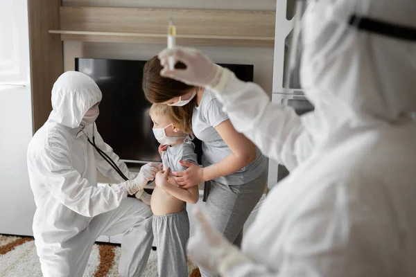 소아과 의사 인그는 얼굴에 마스크를 쓰고 보호용 양복을 입은 병든 아이를 진찰 한다. 엄마 랑 집에 있는 아픈 아이. 아이들 이 집에서 바이러스 치료를 합니다. 코로나 바이러스 대유행. Covid-19 outbreak — 스톡 사진