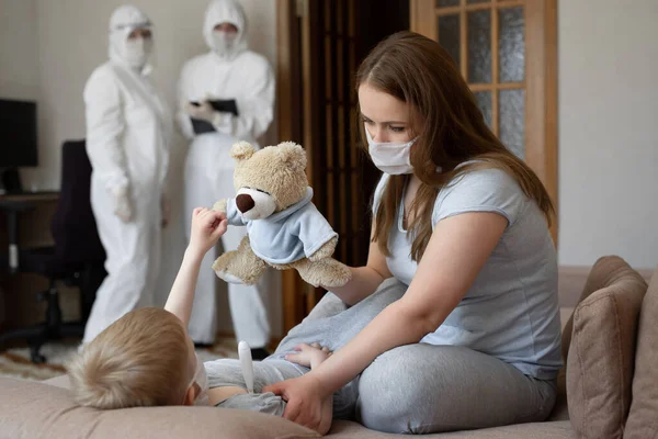 Mama misst die Temperatur der Babys. Ärzte in Schutzanzügen bei kranken Patienten zu Hause. Coronavirus, Covid-19 — Stockfoto