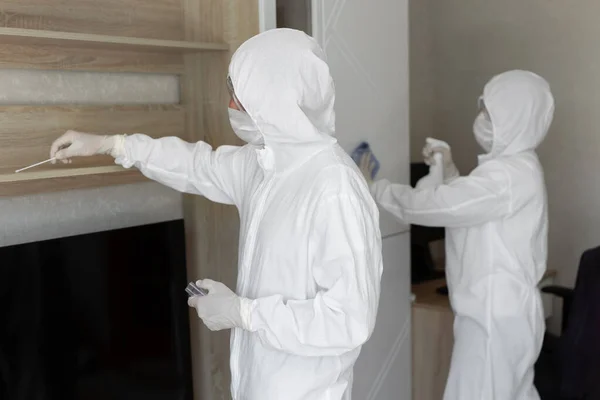 Virologues, les gens en combinaison de protection effectuent la désinfection dans l'appartement. Essuyez les meubles et prélevez des échantillons pour la contamination de la surface pendant une épidémie de coronavirus. Covid - 19 — Photo