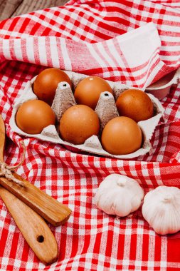 Tahta kepçe, sarımsak ve yumurta kırmızı ve beyaz bir masa halısı üzerinde.