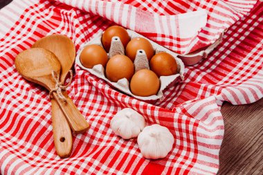Tahta kepçe, sarımsak ve yumurta kırmızı ve beyaz bir masa halısı üzerinde.