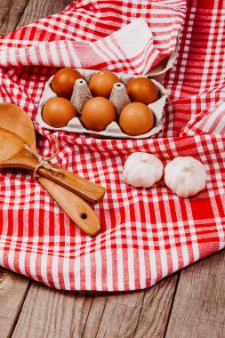 Tahta kepçe, sarımsak ve yumurta kırmızı ve beyaz bir masa halısı üzerinde.