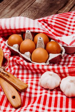 Tahta kepçe, sarımsak ve yumurta kırmızı ve beyaz bir masa halısı üzerinde.